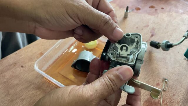 A young man is repairing a small two-stroke engine used for farming. disassemble the parts cleaning the carburetor Reassemble and test 