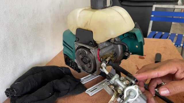 A young man is repairing a small two-stroke engine used for farming. disassemble the parts cleaning the carburetor Reassemble and test 