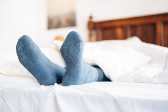 Feet with blue socks sticking out from under the duvet in bed