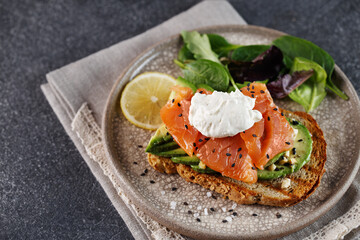 Toast with salmon, cream cheese, avocado, fresh salad on plate