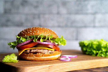 hamburger with cutlet, tomato, cheese and lettuce leaves on a wooden board