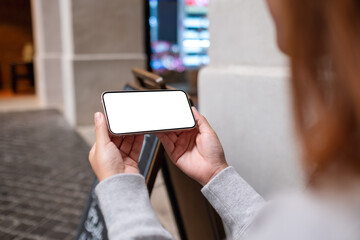 Mockup image of a woman holding and using mobile phone in the outdoors