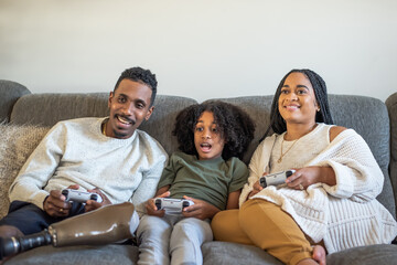 Boy  playing video game with mother and father with prosthetic leg - obrazy, fototapety, plakaty