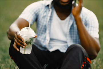 Cropped photo of a black american man sitting on a grass and holding a lemonade