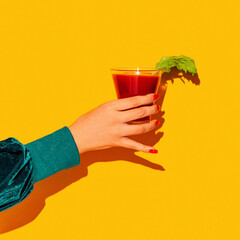 Female hand with bloody mary glass isolated on bright yellow neon background. Concept of taste,...