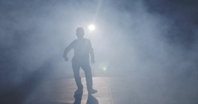 silhouette of a female dancer performing hip hop dance in slow motion with light and smoke background