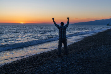 Fototapeta premium silhouette of a man who rejoices in the sea on the seashore in the evening