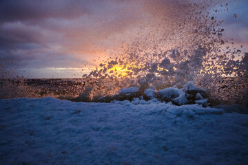 ice splashes at the sea on a cold winter sunset with snow and clouds in the sky