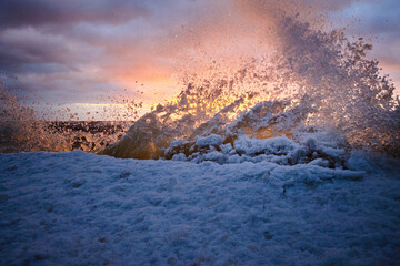 ice splashes at the sea on a cold winter sunset with snow and clouds in the sky