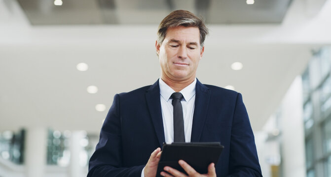 Staying connected in the corporate world. Cropped shot of a mature businessman using a digital tablet while walking through a modern office.