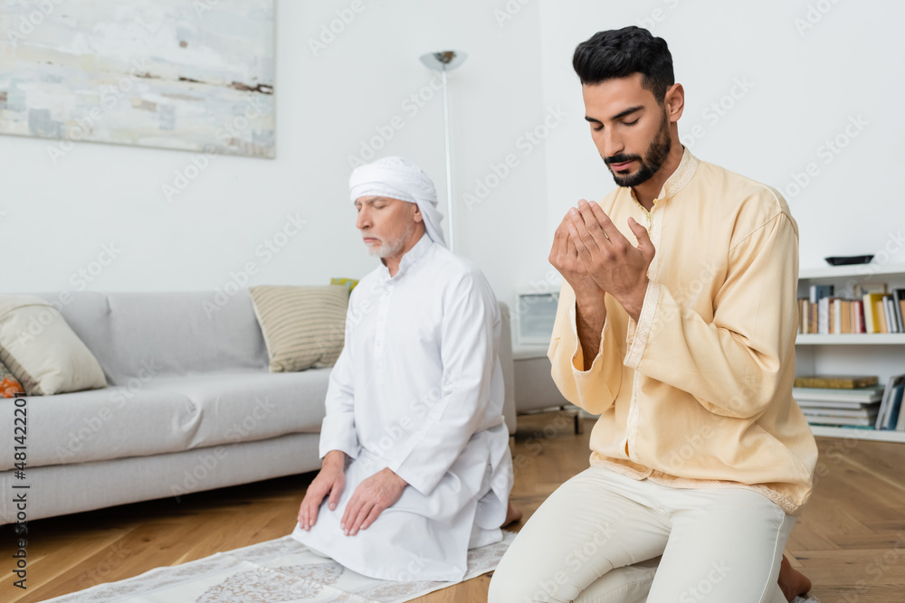 Wall mural middle aged father and arabian son praying at home.