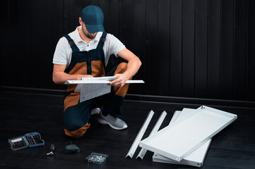 A man in uniform uses the instructions to assemble a white metal shelving in a room or pantry...