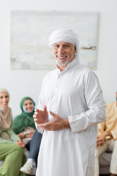 Happy Muslim Man In White Turban Looking At Camera Near Blurred Family.