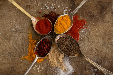 4 metal spoons on a wooden surface and with different spices such as turmeric, smoked paprika,...