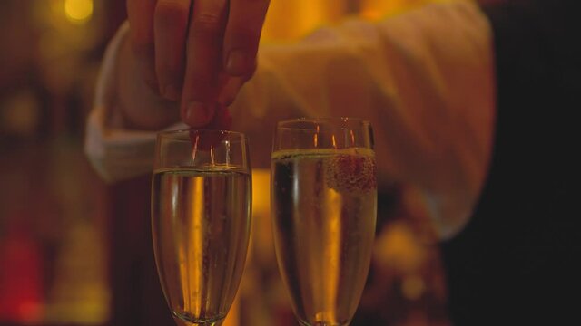 Raspberries dropped into glasses of expensive champagne inside high-end bar in London. The perfect start to a celebration. Luxurious bartending, 5 star service. Bubbles rise in this glass of Prosecco 