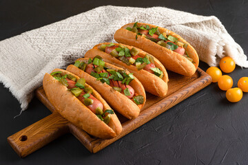 Hot dog, hot dog with pickled cucumbers, jalapeno peppers, carrots, greens on a black background