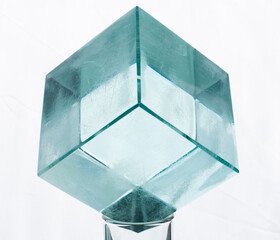 a glass cube on top of a shot glass, in front of a white background.