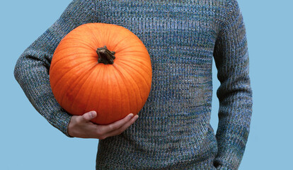 young man holding a big heavy orange pumpkin in his hands on a blue background, halloween...