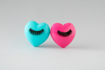 Pink and blue heart with black lashes leaning against each other. Minimalist concept of love and fashion