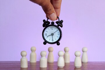 Working hours, hourly wages, deadline concept. Alarm clock and wooden dolls on purple background.