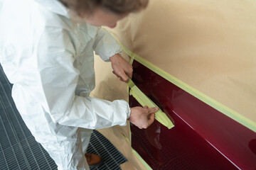Close-up view of auto painter's who masking a car body before painting with masking tape and paper