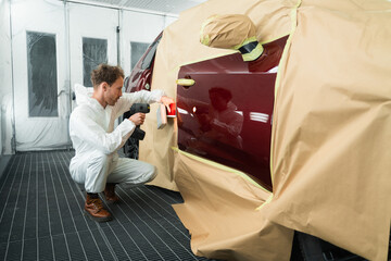 Male colorist compare color sample with car paint using special lamp