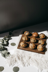 Homemade muffins with blueberries on brown wooden board on white table, boho napkin, leaves, sunlight. Tasty cakes, sweets, cupcakes. No sugar, free gluten. Receipt. Sweet dessert buffet. Mother’s day