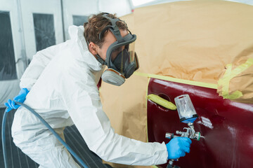 Auto painter in a protective suit and mask sprays a thinner or other cleaner on a car door using a spray gun. Preparation of vehicle body elements for local repair