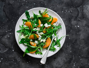 Fruit salad with tangerines, arugula and gorgonzola on a dark background, top view