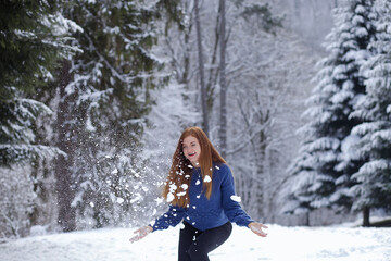 Fototapeta na wymiar winter outside, snow on the road. Against the background of the Christmas tree, a woman plays, in a blue sweater, throws snow
