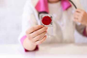a female doctor of European appearance holds a red condom in her hand to fight AIDS. the concept of sexual health