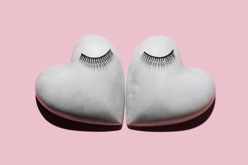 Two concrete/plaster hearts with eyelashes makeup on pastel pink background. Minimalist Valentines Day Concept. Love background.