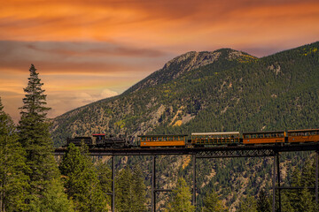 A vintage steam locomotive with tourist passenger cars on a high bridge on the Georgetown Loop...