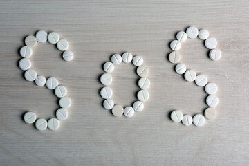 white pills laid out in a word SOS on a table