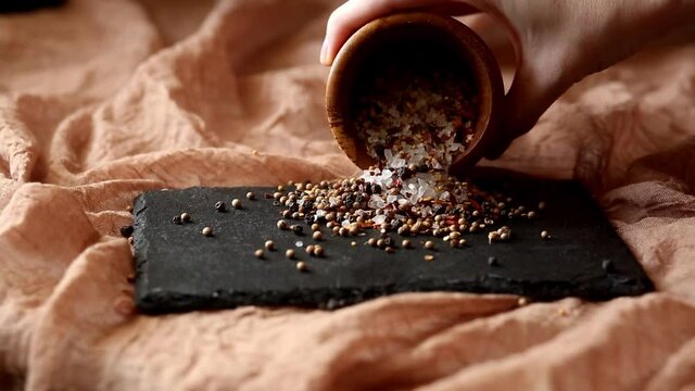 Seasoning - a mixture of pepper and coarse salt is poured from a mortar on a black board on a brown background. Adds flavor to food while cooking