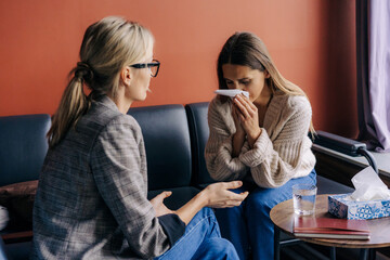 Female patient sitting on sofa and crying while psychotherapist consoling and advising during...