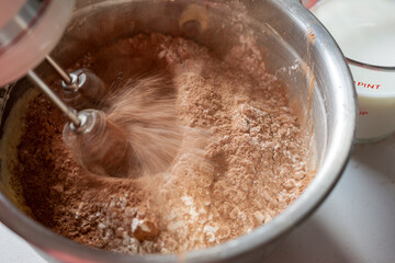 Making of a chocolate cake:  Adding dry ingredients.  Mixer beaters in motion with motion blur.