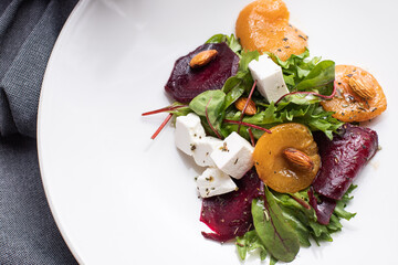 salad with herbs, cheese, nuts, dried apricots, nuts, beets, on a white plate, gray background