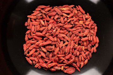 Dried organic goji berries in a black ceramic bowl, macro, top view.