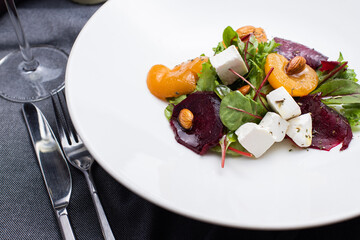 salad with herbs, cheese, nuts, dried apricots, nuts, beets, on a white plate, gray background