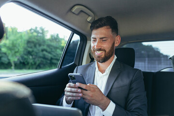 Happy and successful male businessman car passenger reads the news from the phone, rejoices in the victory and the news received