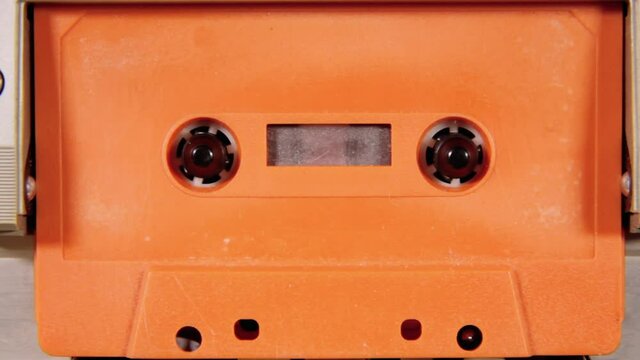 Playing, stopping and removing an old orange unlabeled cassette tape from a deck. Retro vintage worn magnetic media, nostalgic vibes. Front shot.
