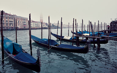 Fototapeta na wymiar Gondeln liegen im Wasser des Canale Grande in Venedig und auf der gegenüber liegenden Seite sieht man venezianische Paläste und den Campanile des Markusdomes in den Hochnebel hinein ragen.