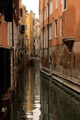 Fototapeta na wymiar Ein Wasserkanal zwischen typischen Häusern und Palästen von Venedig bei Nebligen Wetter. Weiter weg quert eine Brücke den Kanal und zwei Personen laufen gerade darüber hinweg.
