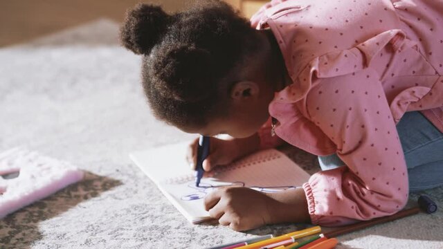 Little African girl drawing something on the floor at home