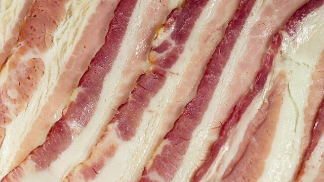 Closeup of slices of raw bacon rotating.