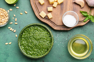 Bowl of tasty pesto sauce and ingredients on green background