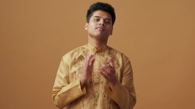 Confident Indian man in national cloth clapping hands in the orange studio