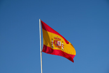 Spanish national flag waving on blue sky background. The flag on a flagpole flutters in the wind. Red with yellow Spain Flag blowing in the wind against on blue sky