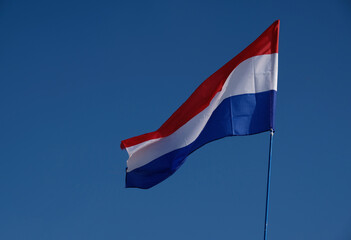 National flag of the Netherlands with horizontal tricolour of red, white and blue. Dutch flag on a flagpole flutters in the wind on blue sky background.